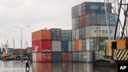Seorang pria berjalan menuju tumpukan kontainer saat banjir rob di Pelabuhan Sunda Kelapa, Jakarta, 7 Desember 2021. (AP Photo/Tatan Shuflana)