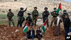 File - Palestinians hold flag in front of Israeli forces during clashes as they protest against Israeli Jewish settlements, in the village of Beit Dajan near the West Bank city of Nablus, Nov. 27, 2020.