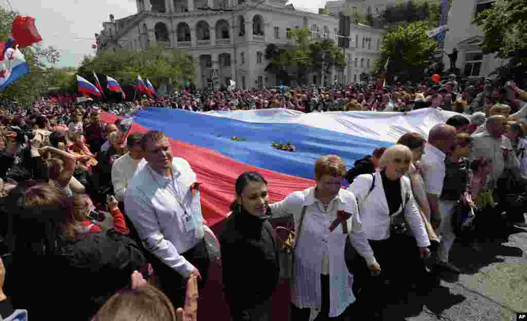 Local residents carry a giant Russian flag as they march through the city after the Victory Day military parade in Sevastopol, Crimea.