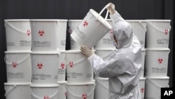 A worker in protective gear stacks plastic buckets containing medical waste from coronavirus patients at a medical center in Daegu, South Korea, Feb. 24, 2020. 