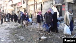Civilians carry their belongings as they walk towards a meeting point to be evacuated from a besieged area of Homs, Syria, Feb. 7, 2014. 