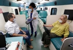 Phlebotomist Sabrina Famiglietti, center, has Miami-Dade County Commissioner Xavier Suarez, left, and wife Rita, right, look over information as they prepare to donate blood aboard a OneBlood blood donation bus, Wednesday, April 22, 2020, in Miami.