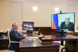 Russian President Vladimir Putin listens to Russian Prime Minister Mikhail Mishustin, displayed on TV screen on the right, during their meeting via teleconference at the Novo-Ogaryovo residence outside Moscow, Russia, April 30, 2020.