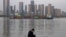 In this Monday, April 13, 2020, photo, a man wearing a mask against the new coronavirus checks his phone as a container ship cruises along the Yangtze River in Wuhan in Central China's Hubei province. China's exports fell further in March compared…