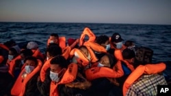 ARCHIVO - Una mujer sostiene a un bebé de 3 meses mientras migrantes y refugiados de diferentes nacionalidades africanas esperan ayuda en un bote de goma abarrotado, el 12 de febrero de 2021, en aguas internacionales del Mar Mediterráneo a 122 millas de la costa de Libia.