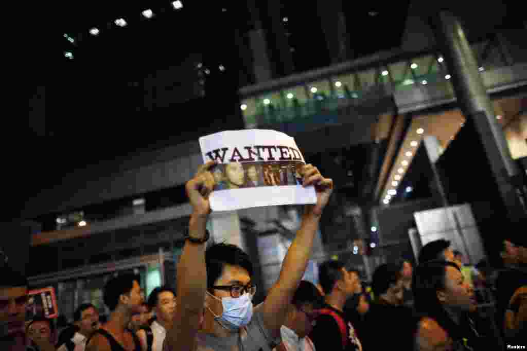 A pro-democracy demonstrator holds a sign with pictures of police officers suspected of beating a protester at a rally last night, as he blocks the entrance of police headquarters at Wan Chai district in Hong Kong, Oct. 14, 2014. 