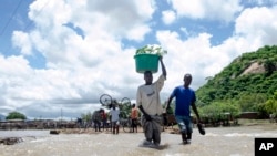 FILE - People cross a river with their belongings where a bridge once stood in Phaloni, Southern Malawi, Jan 22, 2015.