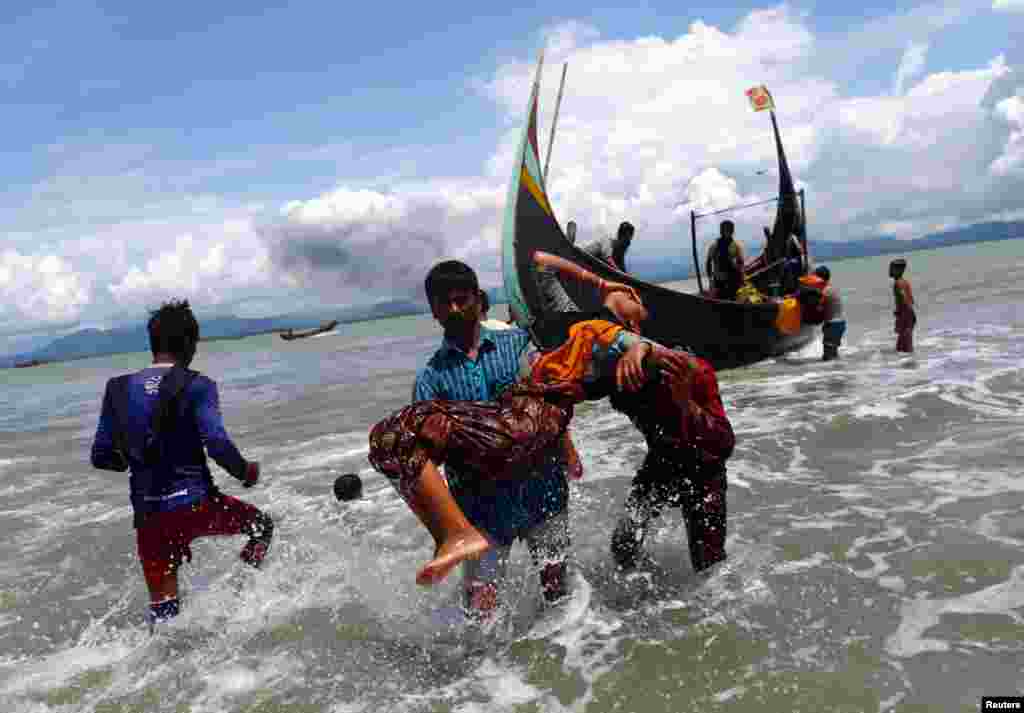 An exhausted Rohingya refugee woman is carried to the shore after crossing the Bangladesh-Myanmar border by boat through the Bay of Bengal, in Shah Porir Dwip, Bangladesh.