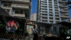FILE - A man walks by a fruits vendor waiting for customers outside a luxury housing construction site in Beijing, Sept. 24, 2024. 