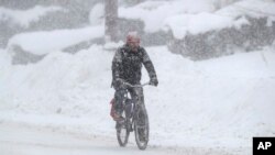 A man rides on his bicycle as fresh snow falls, Dec. 29, 2017, in Erie, Pa.