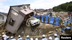 Les secouristes recherchent des personnes disparues dans une maison endommagée par de fortes pluies dans la ville de Kumano, préfecture d'Hiroshima, Japon, le 9 juillet 2018.