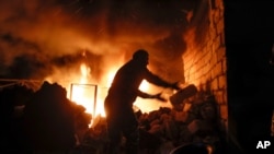 People try to remove car tires from a burning car shop after shelling by Azerbaijan's artillery during a military conflict in Stepanakert, the separatist region of Nagorno-Karabakh, Oct. 23, 2020. 