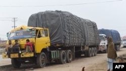 Pakistani drivers sit on the bumper of a loaded truck parked with other trucks along a road near the Wagah border between Pakistan and India on Feb. 20, 2019.