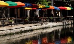 A woman uses her cell phone at a restaurant that remains closed along the River Walk in San Antonio, April 30, 2020. Texas Gov. Greg Abbott is allowing stay-at-home orders to expire Thursday, but San Antonio has extended the orders through May 19.