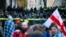 Protesters with a Georgian national flag stand in front of police blocking the entrance of the Parliament's building during a rally to demand new parliamentary elections in the country, in Tbilisi, Georgia, Nov. 25, 2024. 