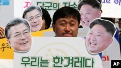 An activist with cutouts of South Korean President Moon Jae-in, left, and North Korean leader Kim Jong Un participates in a rally welcoming the planned summit between South and North Korea in Seoul, South Korea, April 25, 2018. The signs read: "We Are A Nation."