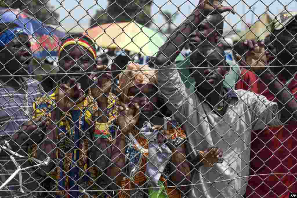 Warga berdiri di belakang gerbang bandar udara M'Poko di Bangui, melihat makanan dikeluarkan dari pesawat kargo.
