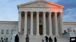 People stand on the plaza in front of the Supreme Court at sunset, Feb. 13, 2016, in Washington. 