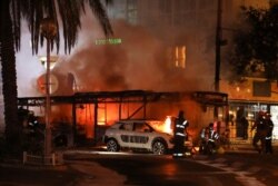 Israeli firefighters, security and rescue forces stand next to a burning bus and car that were hit by a rocket fired from Gaza towards Holon, Israel, May 11, 2021.