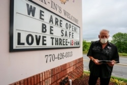 Lester Crowell, managing partner of Three-13 Salon, Spa & Boutique in  Marietta, Ga., changes the letters of the salon's sign, April 24, 2020.