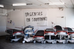 FILE - A picture taken on April 3, 2020 shows a banner reading "Emergency services are suffering" above empty stretchers in the hall of the emergency services of the Aix Hospital Center in Aix-en-Provence, southern France.