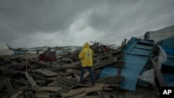In this photo taken Saturday March 16, 2019 and provided by CARE, people walk through the wreckage on the streets of the city of Beira, Mozambique, after Cyclone Idai made landfall. (Josh Estey/CARE via AP)