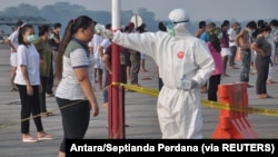 Seorang petugas yang mengenakan alat pelindung memeriksa suhu pekerja migran Indonesia yang tiba dari Malaysia selama karantina untuk mencegah penyebaran COVID-19, sebelum berolahraga di pangkalan udara Soewondo di Medan, Provinsi Sumatra Utara, 11 April 2020.