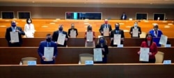 FILE - Members of Arizona's Electoral College stand as they take a photo with signed commemorative copies of the Arizona Presidential Electoral Ballot after casting their votes in the Arizona Electoral College, in Phoenix, Dec. 14, 2020.