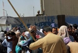 A U.S. soldiers stand inside the airport wall as hundreds of people gather some holding documents, near an evacuation control checkpoint on the perimeter of the Hamid Karzai International Airport, in Kabul, Afghanistan, Aug. 26, 2021.