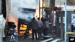In this photo released by the Syrian official news agency SANA, Syrian citizens stand near a burning truck that was destroyed by two cars bombs in a suburb of Damascus, Syria, November 28, 2012.
