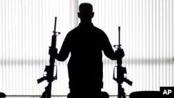 FILE - An agent of the U.S. Bureau of Alcohol, Tobacco, Firearms and Explosives holds guns at an ATF field office in Glendale, Calif., Aug. 29, 2017.