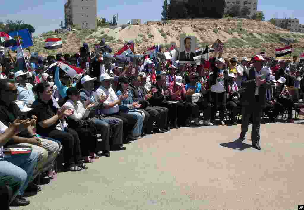 In this photo released by the Syrian official news agency SANA, backers of President Bashar al-Assad hold his portrait and wave Syrian flags during a demonstration in support of his candidacy for another term as president, Damascus, Syria, May 23, 2014.
