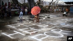 Survivors of Typhoon Haiyan walk over a "Help" message painted on a concrete floor, Saturday, Nov. 16, 2013 in Burauen town, Leyte province, central Philippines.
