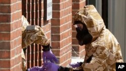 Specialist team members in military protective suits, search for a container feared to be contaminated with traces of the deadly nerve agent Novichok on the fence of John Baker House for homeless people on Rollestone Street in Salisbury, England, July 6, 2018. 