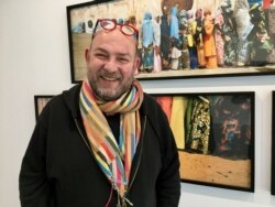 French photographer Eric Guglielmi next to his work on a religious festival in Senegal's holy city of Touba. (Lisa Bryant/VOA)