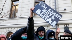 Police officers restrain a supporter of the human rights group International Memorial outside a court building during a hearing of the Russian Supreme Court in Moscow, Dec. 28, 2021. The placard reads: 'We will live forever'.