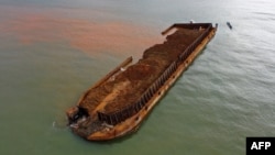 Perahu nelayan di samping tongkang pengangkut nikel yang tenggelam dan mencemari laut di perairan tujuan wisata Pantai Gong di Kabupaten Konawe, Sulawesi Tenggara. (Foto: AFP)