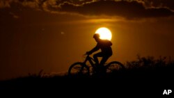 FILE - A cyclist tops a hill on a hot day at sunset, Aug. 20, 2023, in San Antonio. Scientists say 2023 will be the warmest in 125,000 years.