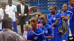 A Liberian school teacher (L) takes the temperature of students arriving for morning lessons at school, as part of the Ebola prevention measures at the BW Harris High School in Monrovia, Feb. 16, 2015.