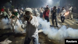 Muslim hardline protesters cover their faces as police fire tear gas during a protest against Jakarta's incumbent governor Basuki Tjahaja Purnama, an ethnic Chinese Christian running in the upcoming election, Nov. 4, 2016.