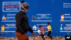 Les gens passent devant des messages de prévention contre le COVID-19 dans le canton de Soweto à l'extérieur de Johannesburg, Afrique du Sud, le 13 juillet 2020.