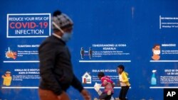 People walk past a COVID-19 advertisement in the township of Soweto outside of Johannesburg, South Africa, July 13, 2020.