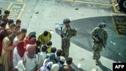 US soldiers stand guard as Afghan people wait at the Kabul airport in Kabul on August 16, 2021, after a stunningly swift end to Afghanistan's 20-year war, as thousands of people mobbed the city's airport trying to flee the group's feared hardline brand…