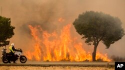 A military police officer stands by his motorcycle next to flames from a forest fire near Mazagon in southern Spain, June 25, 2017.