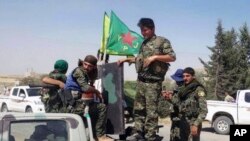 FILE - In this file photo released June 23, 2015, provided by the Kurdish fighters of the People's Protection Units (YPG), Kurdish fighters of the YPG sit on their pickup in the town of Ein Eissa, north of Raqqa city, Syria.