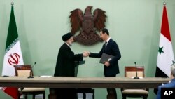 Syrian President Bashar Assad, right, and Iranian President Ebrahim Raisi shakes hands after they sign a cooperation agreement at the presidential palace in Damascus, Syria, May 3, 2023. 