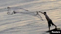 FILE - A man casts a fishing net on the bank of the Mekong river in Phnom Penh. 