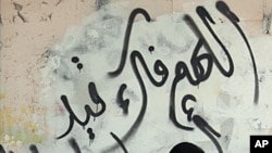 A Bahraini woman shops for produce on Tuesday, October 4, 2011, in the Shi'ite Muslim village of Malkiya, Bahrain. The graffiti on the wall behind her reads: "God, free our prisoners."
