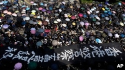 Protesters carrying umbrellas and a huge banner reading "Hong Kong police deliberate murder" march on a street in Hong Kong, Oct. 20, 2019. Authorities are beefing up security ahead of an unauthorized rally by pro-democracy protesters.