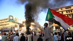 Seorang pria Sudan membawa bendera negaranya dalam aksi protes di ibu kota Sudan, Khartoum, pada 19 Desember 2020, untuk menunjukkan rasa frustrasi akan tidak adanya perubahan yang berarti sejak militer berkuasa pada 2019 lalu. (Foto: AFP/Ashraf Shazly)